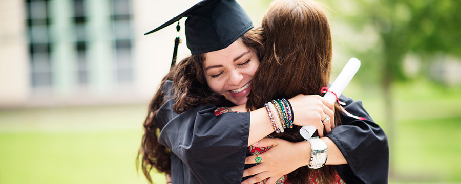 Student in a cap and gown hugging and smiling